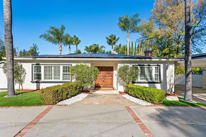 Front exterior of the main residence, with a wood entry door, solar panels, and a palm-lined driveway