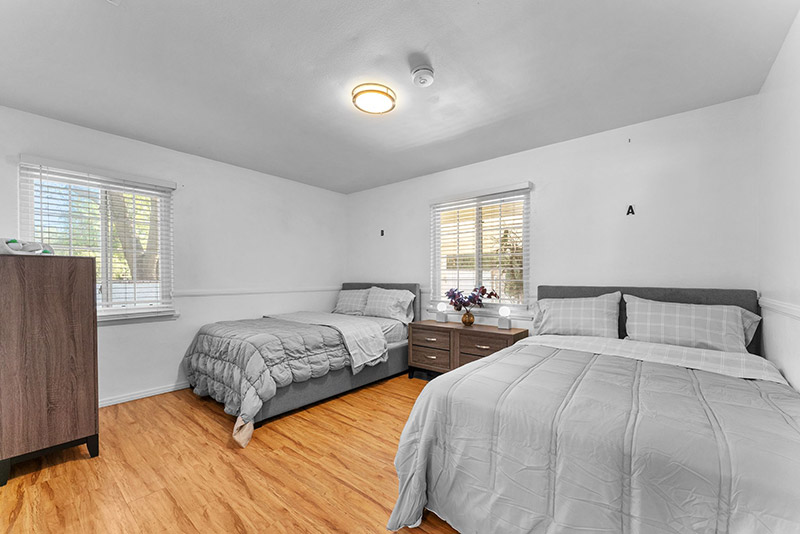 Bedroom with two beds, a nightstand, and natural light from two windows
