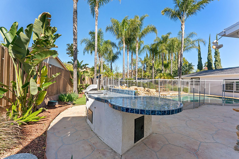 Outdoor kitchen and bar area beside the pool, surrounded by palm trees