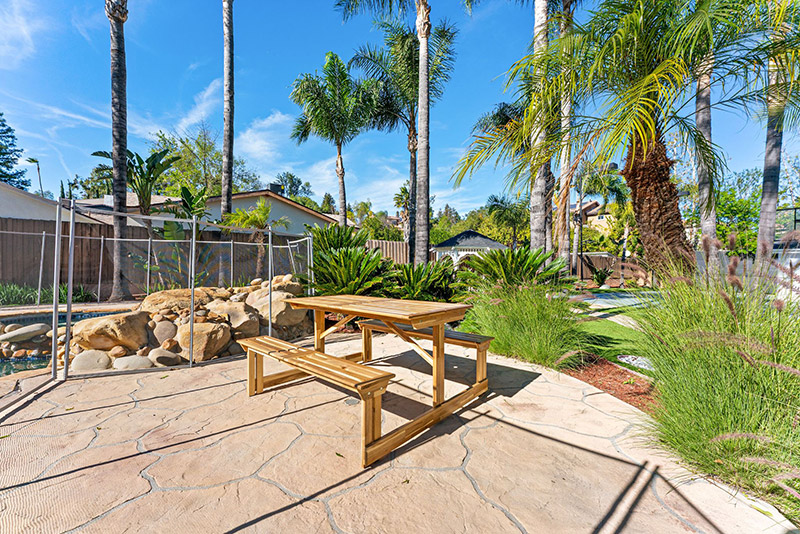 Outdoor picnic table on a stone patio surrounded by palm trees