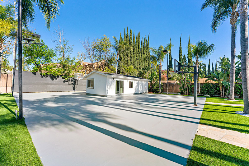 Half basketball court beside a small guest house, framed by palm trees