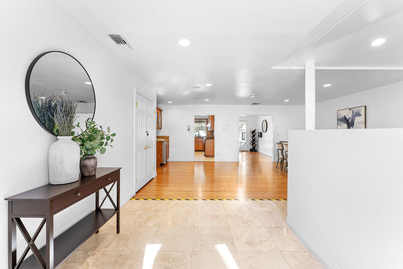 Bright entryway with a round mirror and console table, opening into the home's kitchen and living areas