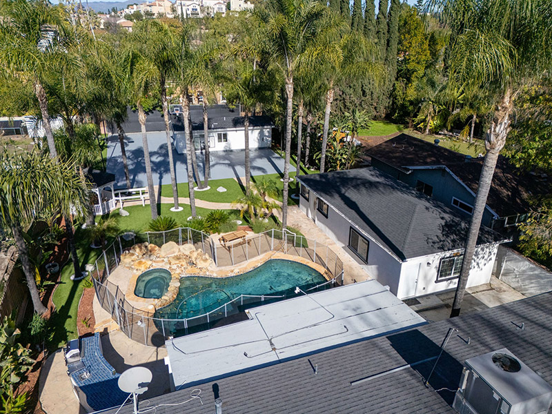 Aerial view of the pool, spa, and covered patio among tall palm trees
