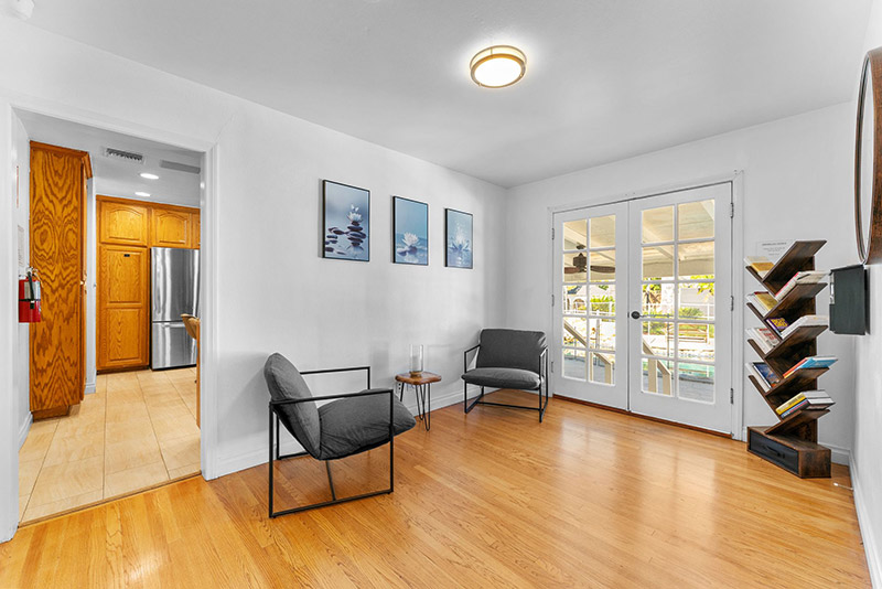 Sitting room with two accent chairs and a bookshelf, with French doors leading out to the pool